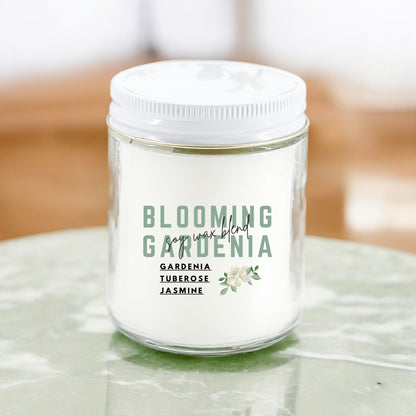 A white candle with the label 'Blooming Gardenia' written on it, set on a marble surface.
