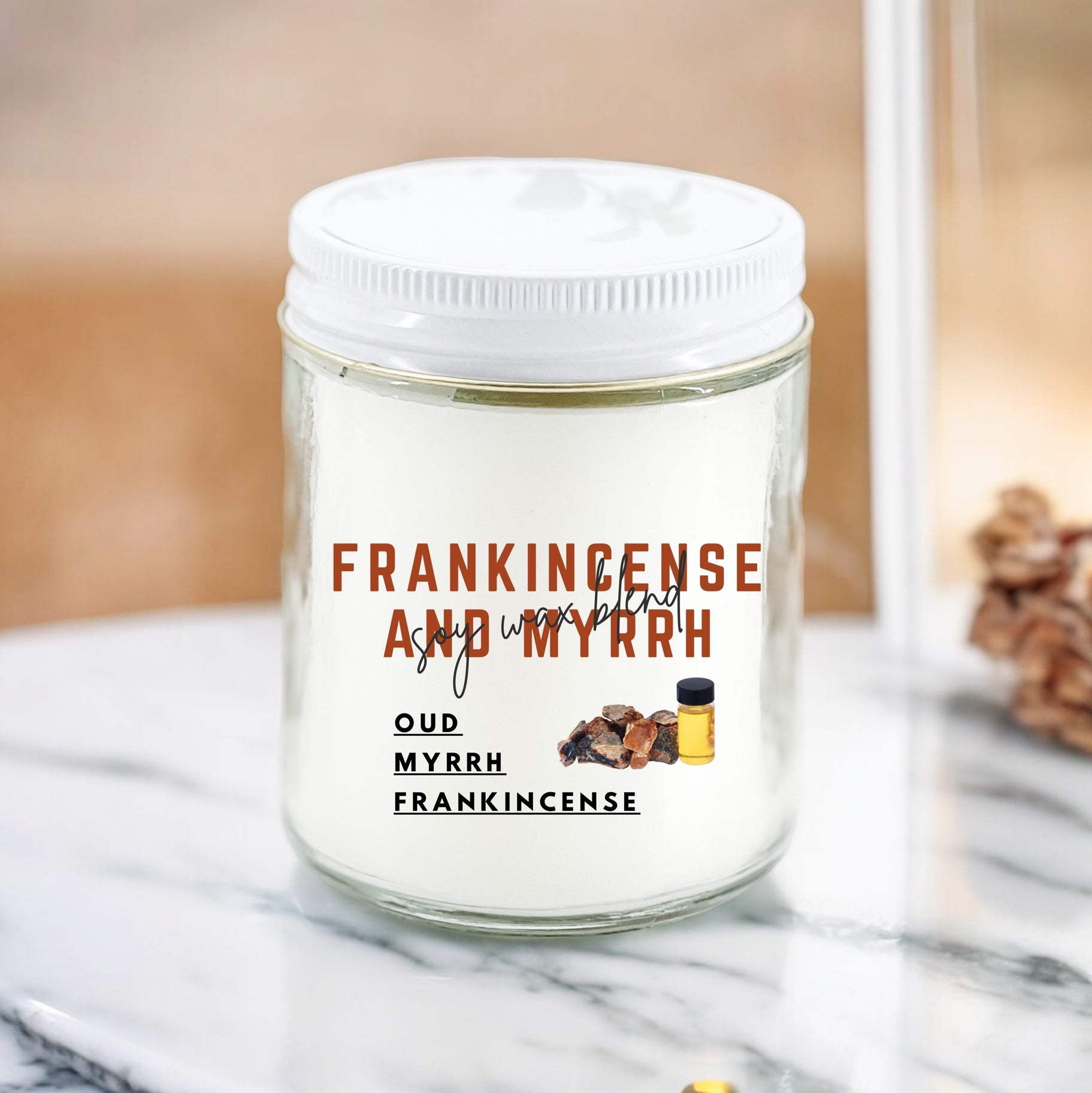 A white candle with the label 'FRANKINCENSE AND MYRRH' on a marble surface, with pine cones and a incense burner in the background.