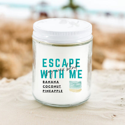 An 8 oz candle with the label 'Escape With Me' featuring the scents Banana, Coconut, Pineapple, placed on a sandy surface with a blurred background.