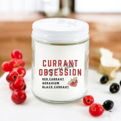 An 8 oz jar candle labeled 'Currant Obsession' with red currants and a slice of lemon in the background.
