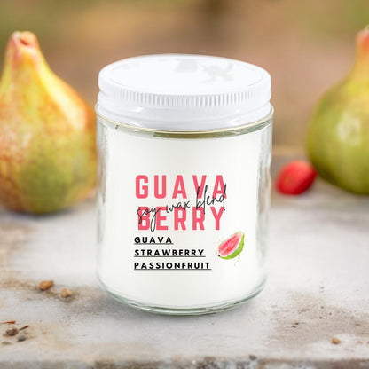 A white candle jar with 'GUAVA BERRY' text and an illustration of a guava on it, set against a backdrop with fruits and a pink flower.