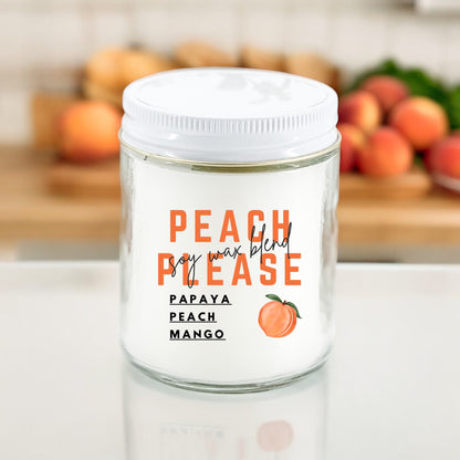 A white candle with the label 'PEACH PLEASE' and additional text 'PAPAYA PEACH MANGO'. The candle is on a kitchen counter with fruits in the background.