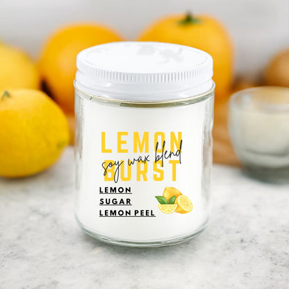 A white jar candle labeled Lemon Burst with lemon and orange decor in the background.